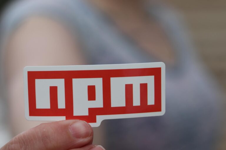 Blurred background close-up of a hand holding an npm sticker, ideal for web development themes.